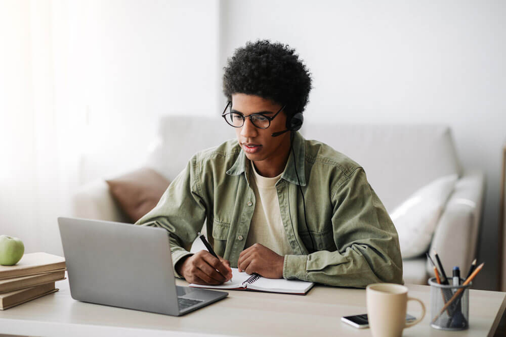 Industrious black teenager in headset studying remotely from home
